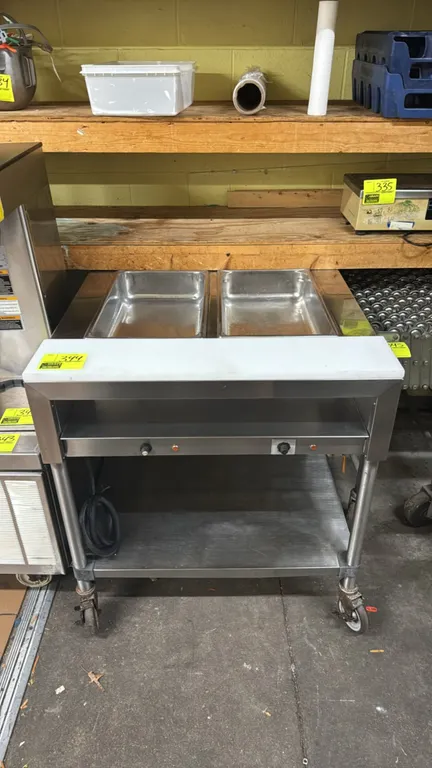 Stainless steel portable 2-well electric steam table. Features (2) heated wells with independent controls, front poly cutting board, recessed storage