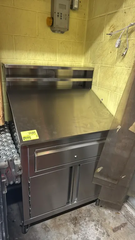 Stainless steel receiving desk. Features a sloped writing surface with upper organizer shelf, single locking drawer with keys, and lower two-door stor