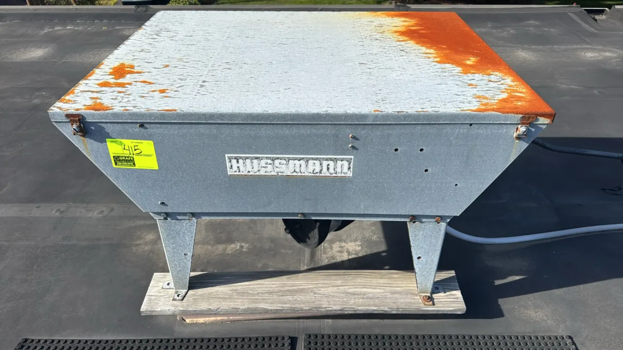 Hussmann rooftop condensing unit. Features galvanized steel housing, finned condenser coil, and elevated leg stands. Note: Heavy rust on top cover.