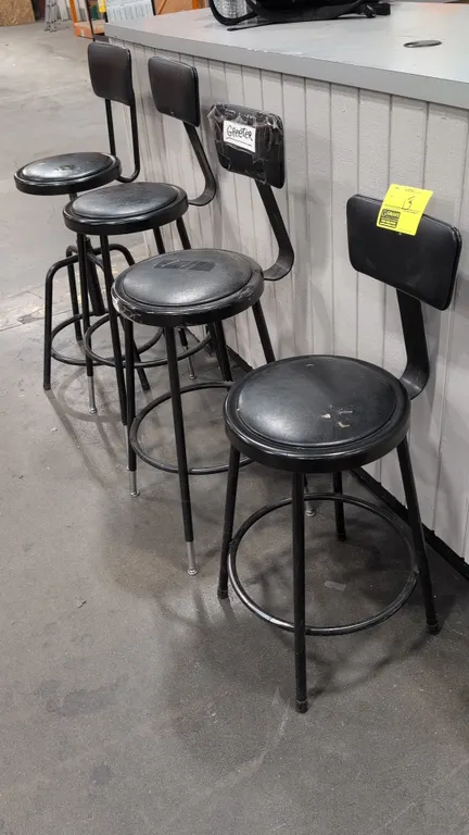Assorted cushioned bar height stools. Features black faux leather upholstered round seats and backrests, tubular metal frames, and integrated ring foo