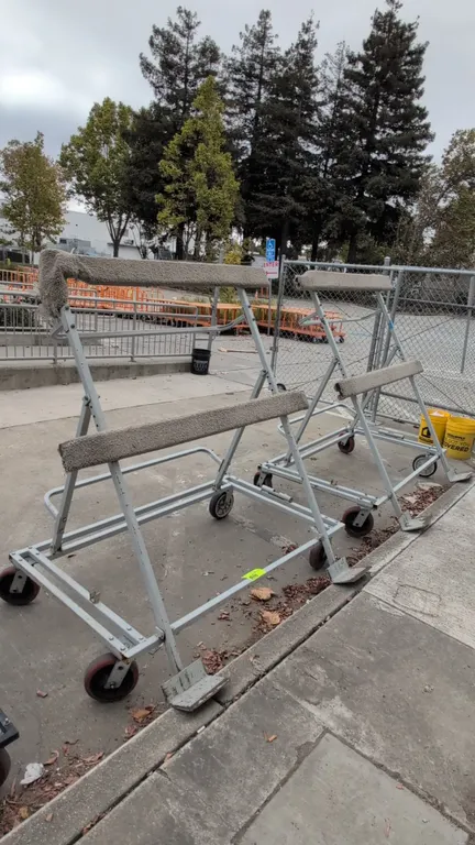 Portable metal flat panel carts. Features carpet-padded horizontal supports, dual bottom resting plates, and rear tubular push handles. 5'L. Mounted o