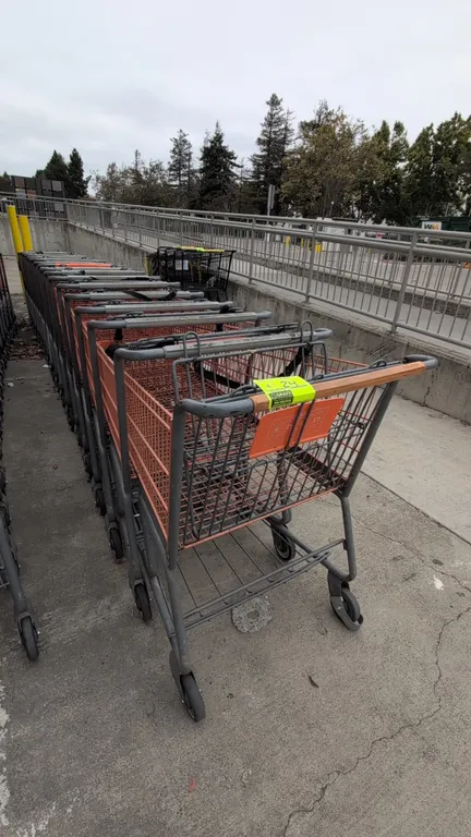 Metal shopping carts. Features orange wire basket with corner bumpers, folding child seat with safety strap, lower wire storage tray, and gray tubular