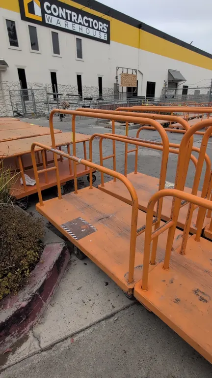 Metal platform lumber cart. Features tubular steel upright dividers and orange finish. 54" x 30". Mounted on casters.