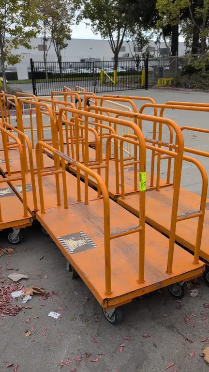 Metal platform lumber carts. Features tubular steel upright dividers and side rails with orange finish. 54" x 30". Mounted on casters.