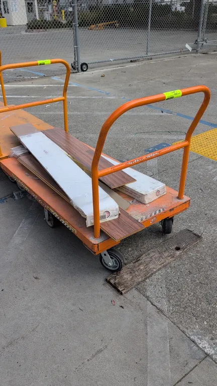 Metal platform cart with TrafficMaster laminate flooring planks. Features orange painted steel deck, tubular push handle, and a 6-wheel caster configu