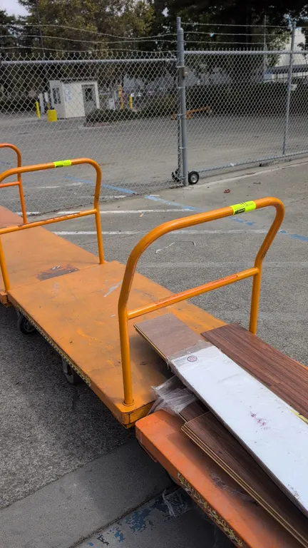 Metal platform cart. Features orange painted steel construction, removable tubular push handle, and a 6-wheel tilt configuration with rigid center whe