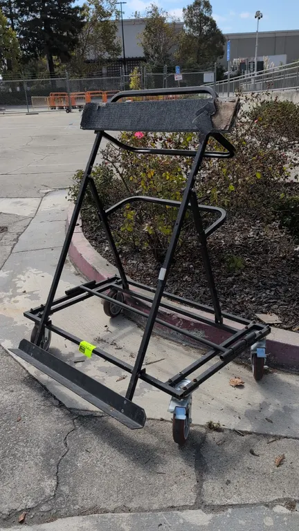 4'L metal portable flat panel cart. Features carpet-padded upper support rail, bottom support ledge, and dual tubular handles. Mounted on swivel caste