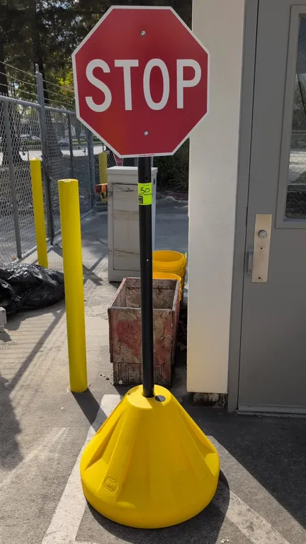 Portable STOP sign with polyethylene rolling base. Features an octagonal reflective stop sign mounted on a black upright pole, yellow molded polyethyl