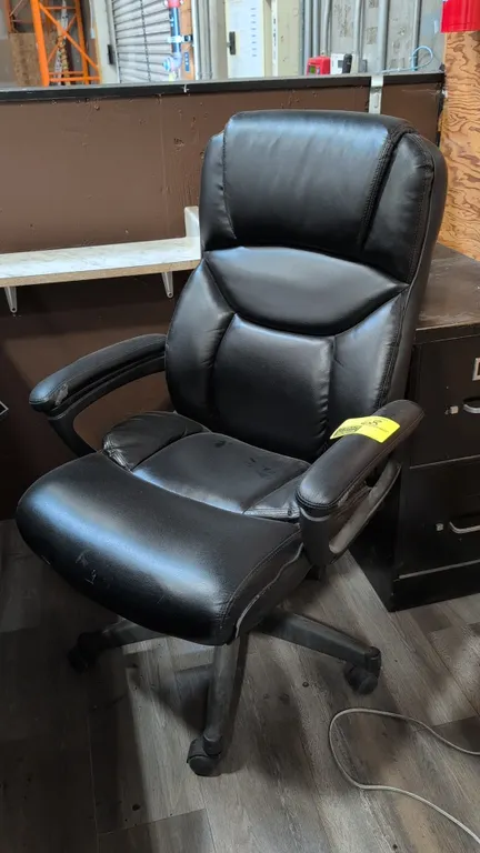 Faux leather cushioned office chair. Features black upholstery, high-back design, padded armrests, and pneumatic height adjustment. Mounted on a 5-sta
