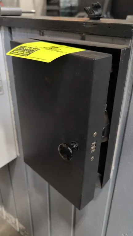 Metal key lock box. Features a 3-digit combination lock, exterior turn knob, and interior key organizer hooks. Wall-mountable black metal construction