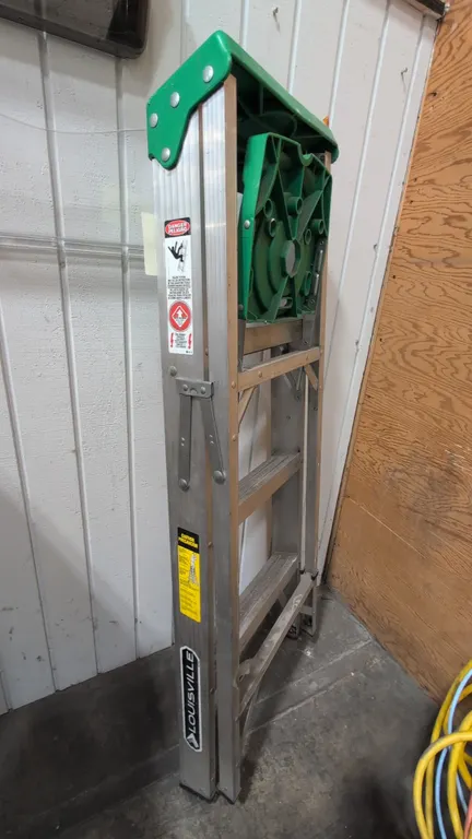 2018 Louisville AS4004 4' aluminum stepladder. Features a molded green top with tool slots, fold-out pail shelf, slip-resistant ribbed steps, and pinc
