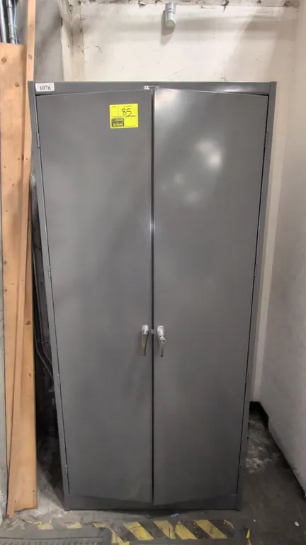 Uline metal 2-door storage cabinet. Features locking handle with key and 4 interior shelves. Finished in gray. Dimensions: 3' x 2' x 6-1/2'. Contents