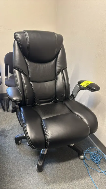 Faux leather padded office chair. Features black faux leather upholstery with contrast stitching, perforated center panels, and flip-up padded armrest