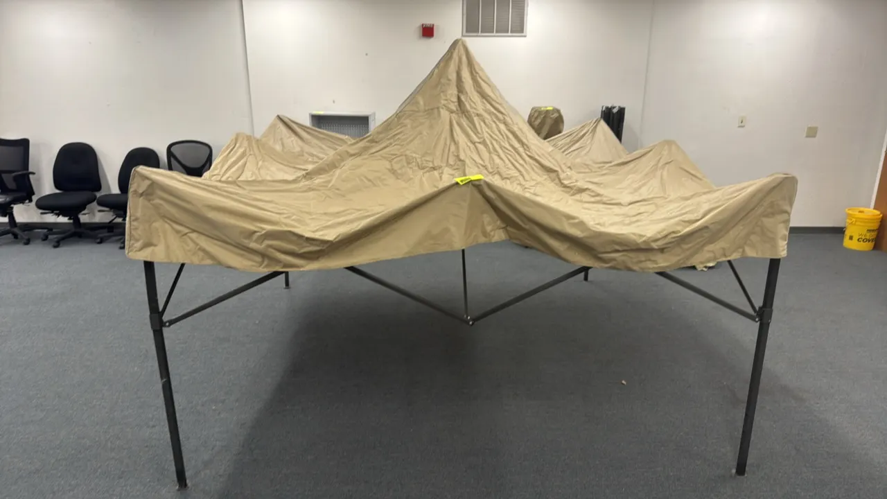Approximately 10' x 10' metal pop-up canopy. Features collapsible metal frame and tan fabric canopy top. Note: Canopy is not fully erected. Background