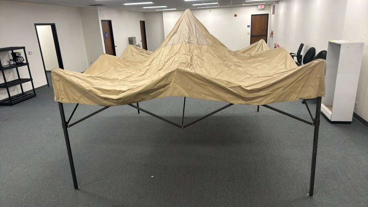 Metal pop-up canopy tent. Features a folding metal frame with a tan fabric canopy top. Approximately 10' x 10'. Background items not included.