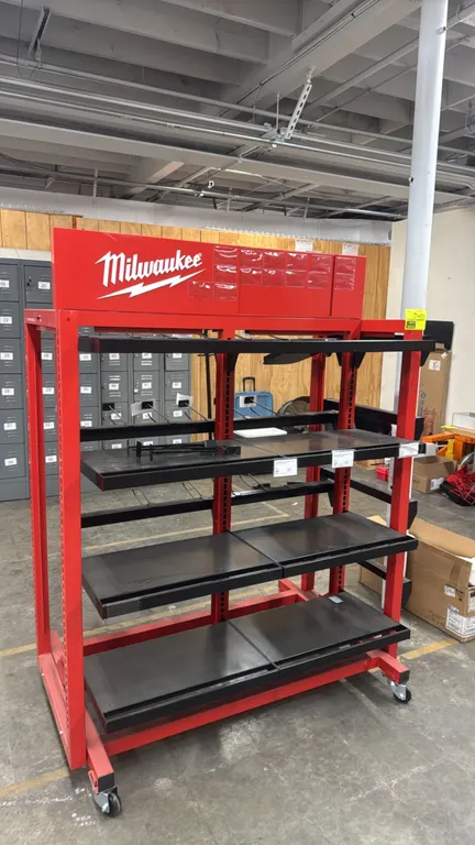 Milwaukee metal portable 4-way merchandiser display rack. Features Milwaukee branded top header, adjustable shelves, display trays, and hanging hooks.