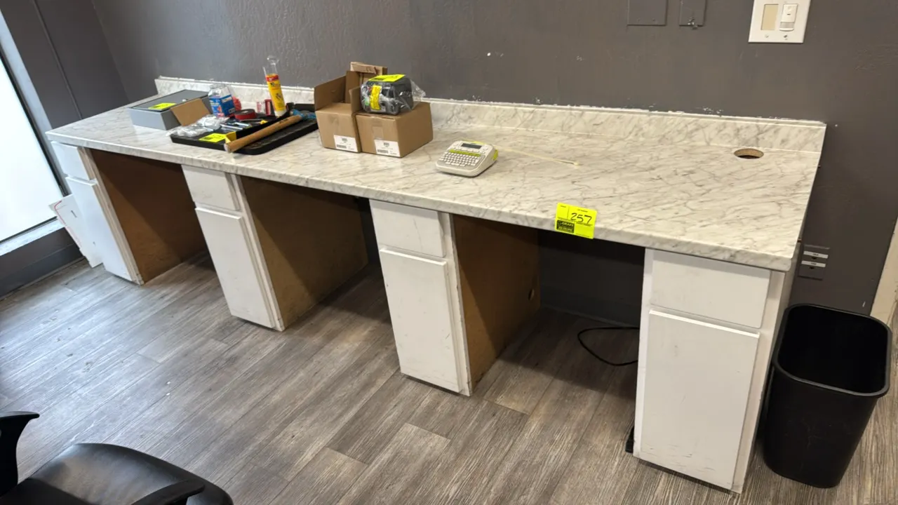 Laminate counter workstation with lower cabinets. Features faux marble laminate top with backsplash, cable pass-through grommet hole, and four base ca