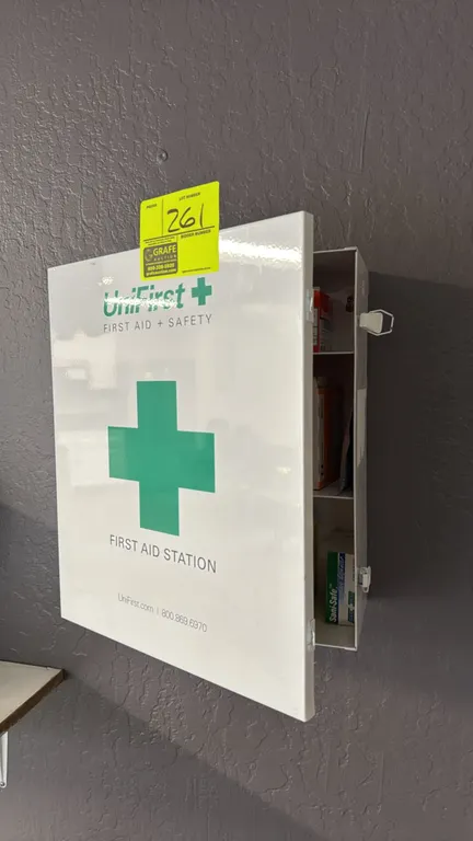 UniFirst metal first aid station cabinet. Features white metal construction, single hinged door with latches, three interior storage compartments, and