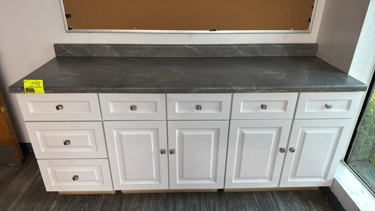 Base cabinet with laminate countertop. Features white finish, raised panel doors and drawer fronts, brushed metal pulls, 7 drawers, and 4 cabinet door