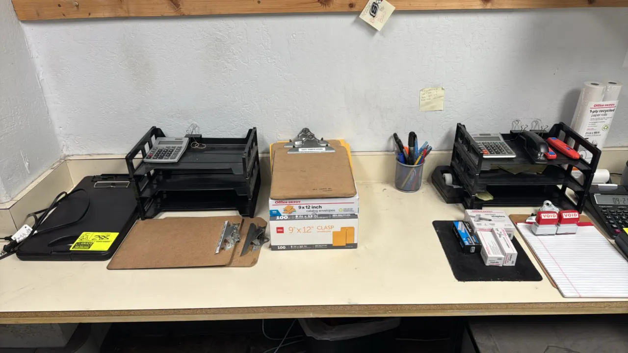 Assorted office supplies. Includes stackable plastic desk trays, hardboard and plastic clipboards, desktop calculators, a stapler, tape dispenser, box