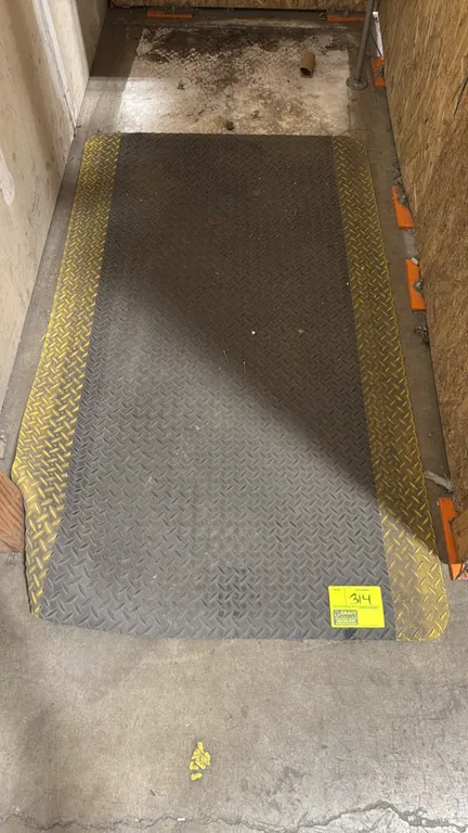 Anti-fatigue floor mat. Features black diamond plate embossed traction surface, high-visibility yellow safety borders, and beveled edges. 5'L.