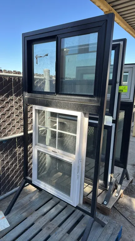Window sample display stand with windows. Features a black metal freestanding frame holding a horizontal sliding window and a single-hung window with