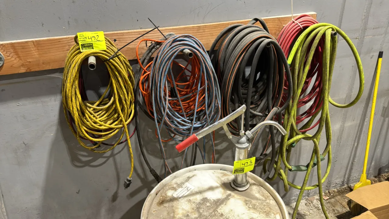 Wall-mounted hose and cord rack with assorted extension cords and hoses. Features a wood mounting board with metal pipe pegs. Includes various electri