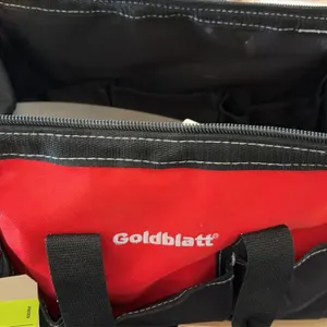 Goldblatt tool bag with assorted masonry hand tools. Includes masonry brush, 11" x 5-1/2" trowel, clamps, and related accessories. Bag features heavy-