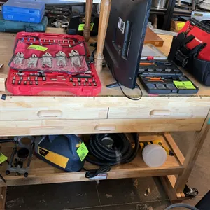 Wood double-sided workbench. Features hardwood construction, integrated wood vise, drawers on both sides, and a lower storage shelf. Includes contents