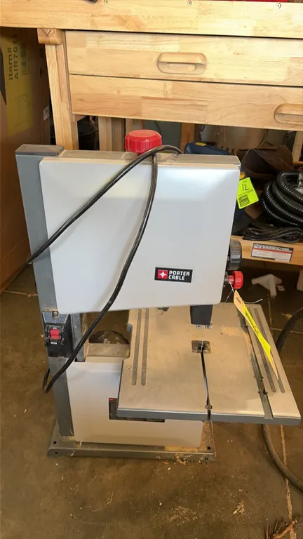 Porter-Cable benchtop band saw. Features an adjustable metal work table, rear-mounted electric motor, and front power switch. Attached power cord.