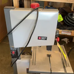 Porter-Cable benchtop band saw. Features an adjustable metal work table, rear-mounted electric motor, and front power switch. Attached power cord.