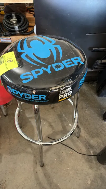 Spyder shop stool. Features a round padded vinyl seat with Spyder and Lowe's Pro branding. Mounted on a chrome tubular steel frame with a circular foo