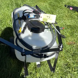 Brinly 12-gallon pull-behind boom sprayer. Features a translucent polyethylene tank, rear spray boom, hand spray wand with hose, and an Everflo 12V el