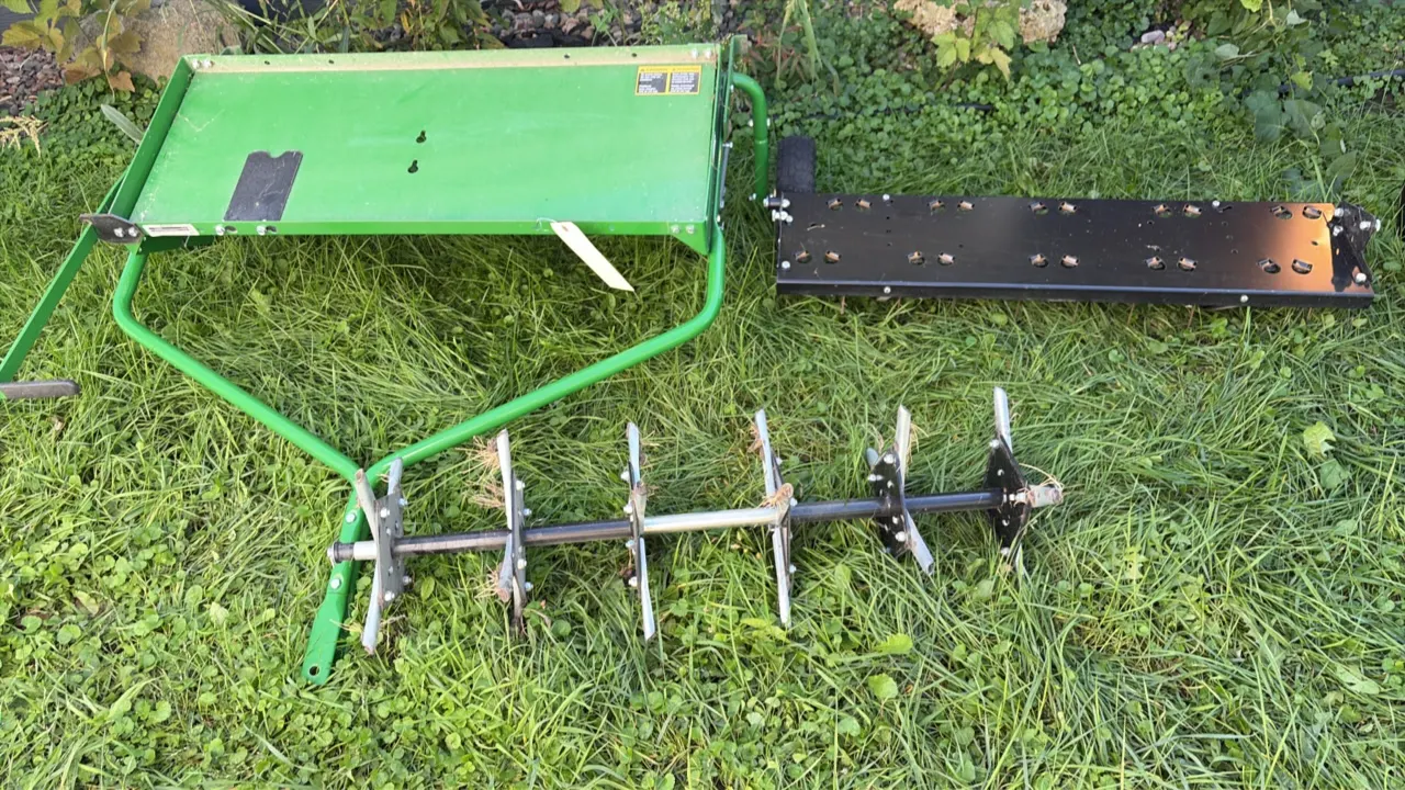 John Deere tow-behind lawn aerator and dethatcher. Includes weight tray platform frame with pin hitch, plug aerator coring tine assembly, and spring t