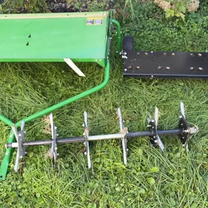 John Deere tow-behind lawn aerator and dethatcher. Includes weight tray platform frame with pin hitch, plug aerator coring tine assembly, and spring t