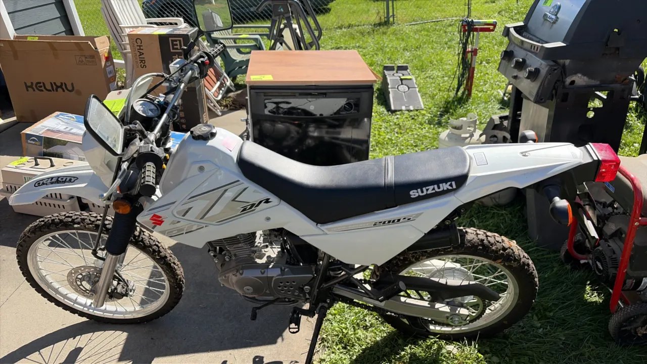 Suzuki DR200S dual-sport motorcycle. Features white body panels, spoked wheels, front disc brake, rear drum brake, dual mirrors, headlight, taillight,