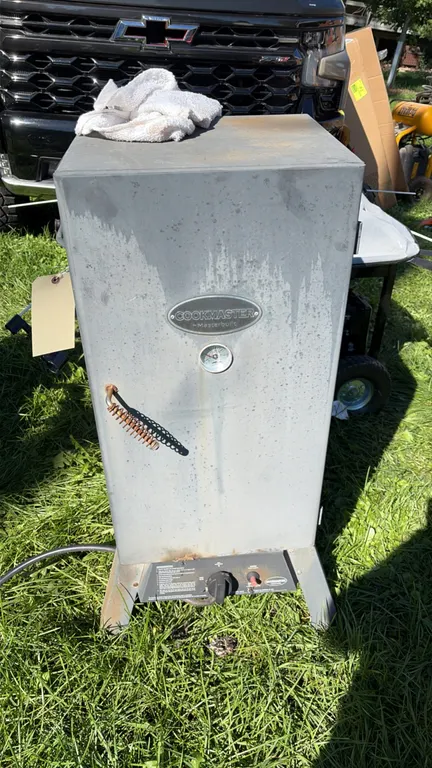 Masterbuilt Cookmaster vertical propane smoker. Features door-mounted temperature gauge, wire spring door handle, push-button igniter, internal wire c