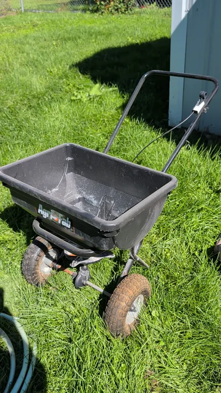 Agri-Fab push broadcast fertilizer spreader. Features a poly hopper, handle-mounted flow control lever with cable linkage, rotating broadcast impeller