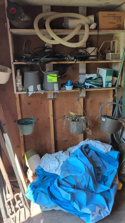 Assorted storage shed contents. Includes pool filter pump with hoses, inflatable pool liner, metal bed frame rails, garden fork, hanging and plastic f