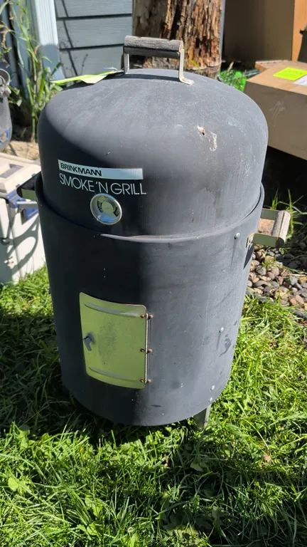Brinkmann Smoke 'N Grill vertical smoker. Features dome lid with wooden handle, temperature indicator, front access door, wooden side handles, and int