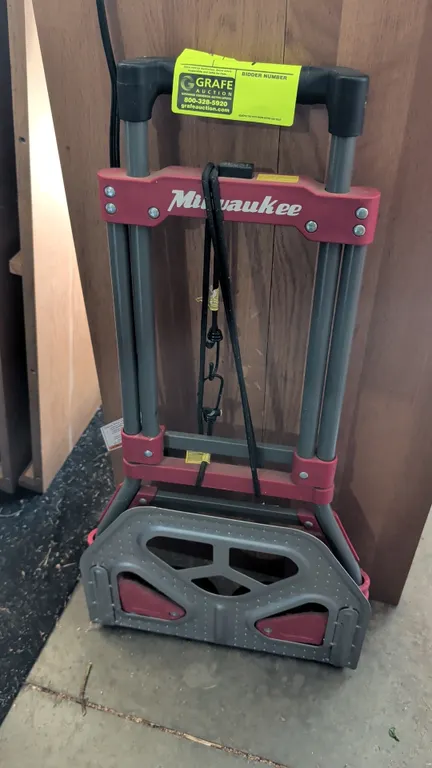 Milwaukee collapsible hand truck. Features a telescoping handle, folding aluminum toe plate, folding wheels, and included bungee cord. Capacity: 150 l