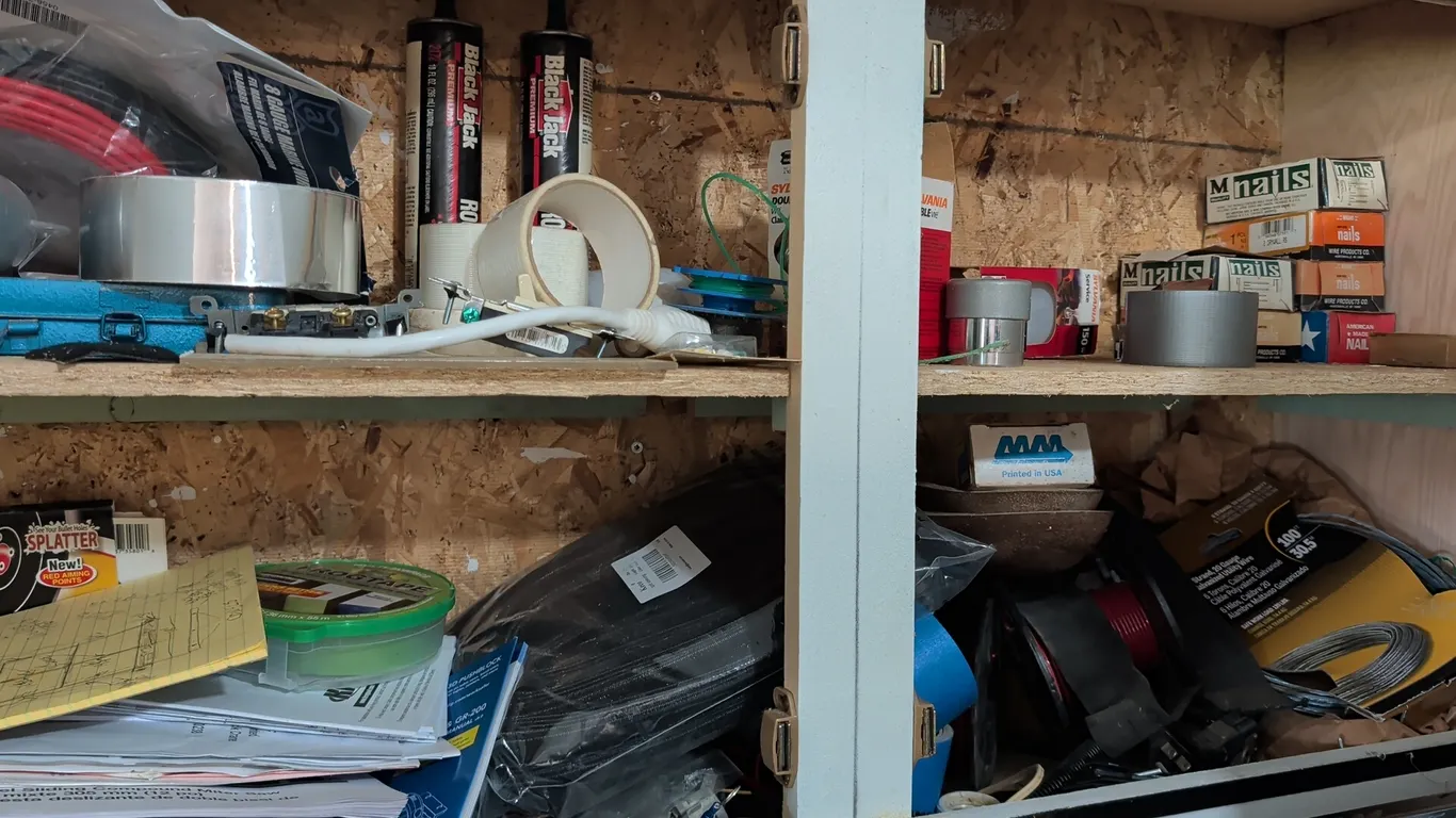 Assorted cabinet contents. Includes electrical wiring and utility wire, boxed nails, Black Jack roof sealant tubes, assorted rolls of tape, light bulb