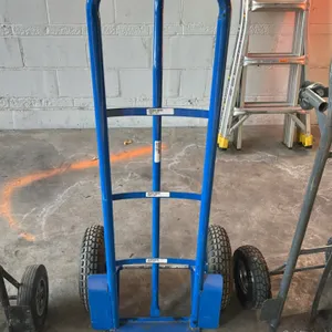 Steel 2-wheel hand truck. Features a blue tubular frame, continuous loop handle, vertical center support strap, integrated wheel guards, and pneumatic