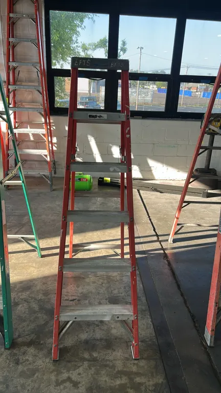 Louisville 6' stepladder. Features orange fiberglass rails, aluminum steps, and a molded top cap. Note: Background ladders and equipment not included.