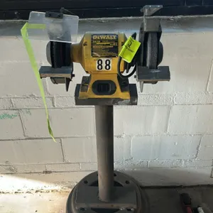 DeWalt DW758 8" bench grinder. Features adjustable tool rests, left clear eye shield, grinding wheel, and wire wheel. Mounted on a steel pedestal stan