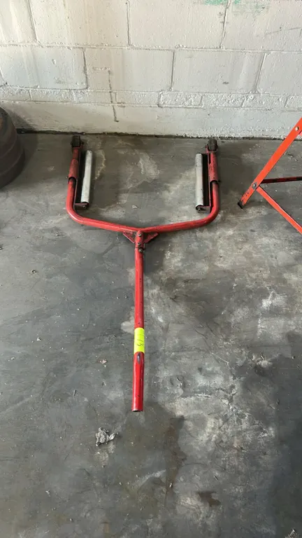 Truck tire and wheel dolly. Features red tubular steel frame construction, dual rotating steel roller assemblies, two wheels, and an extended leverage