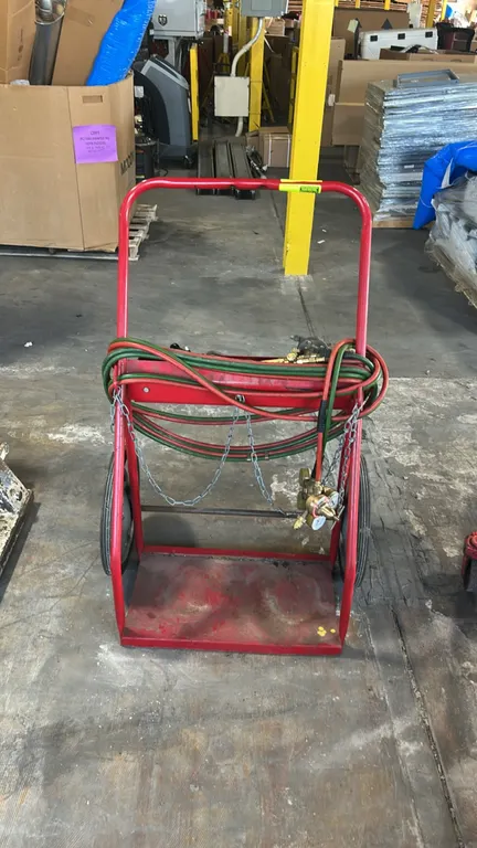 Dual-cylinder welding and cutting torch cart. Features tubular steel frame with red finish, base platform with retention chains, and storage tray. Inc