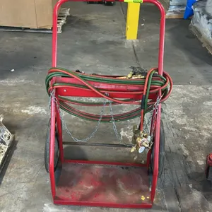 Dual-cylinder welding and cutting torch cart. Features tubular steel frame with red finish, base platform with retention chains, and storage tray. Inc