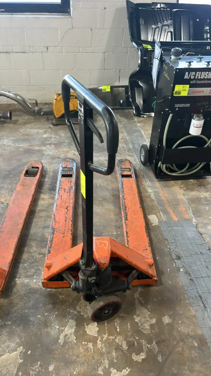 Manual hydraulic pallet jack. Features steel construction with orange finish, ergonomic loop handle with integrated release lever, tandem load rollers
