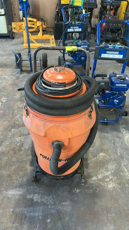 Pullman-Holt 102 commercial vacuum cleaner. Features flexible vacuum hose, crevice tool attachment, bottom tank drain valve, and integrated power cord